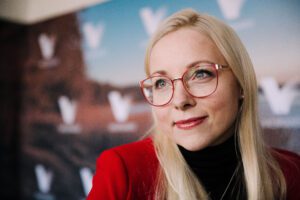 Dr. Maarja Merivoo-Parro, a blonde woman with red frame glasses, looks off camera.