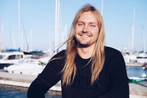 A man with long blonde hair smiles at the camera